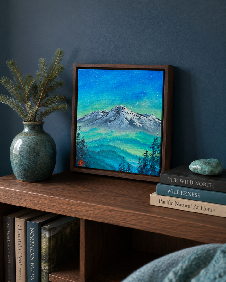 A framed landscape painting of a snowy mountain under a vibrant blue and green night sky, styled on a wooden shelf next to a ceramic vase with pine branches and a stack of books.