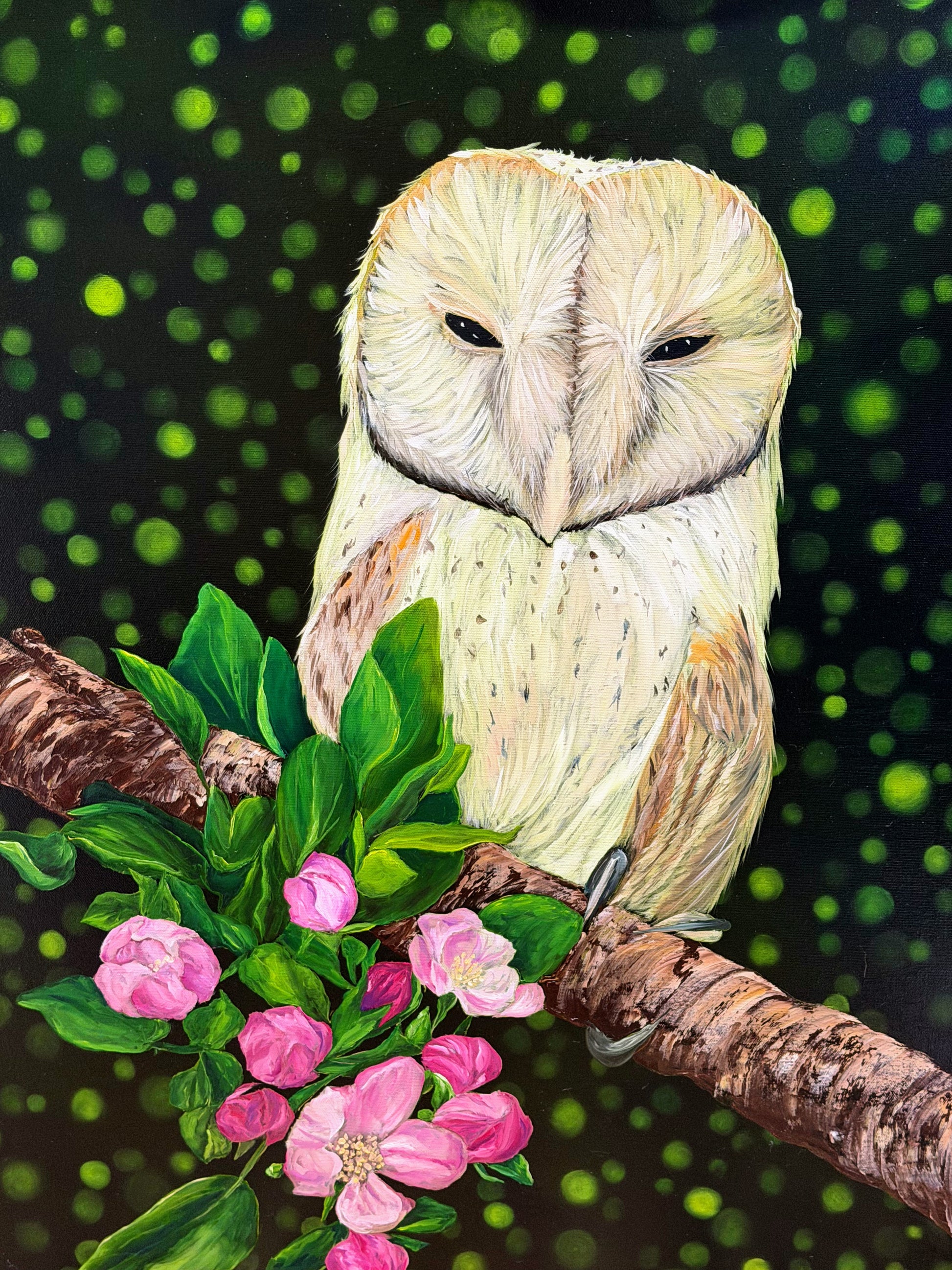 A painted barn owl perched on a branch with pink blossoms and green leaves, set against a dark background with glowing green bokeh-like lights.