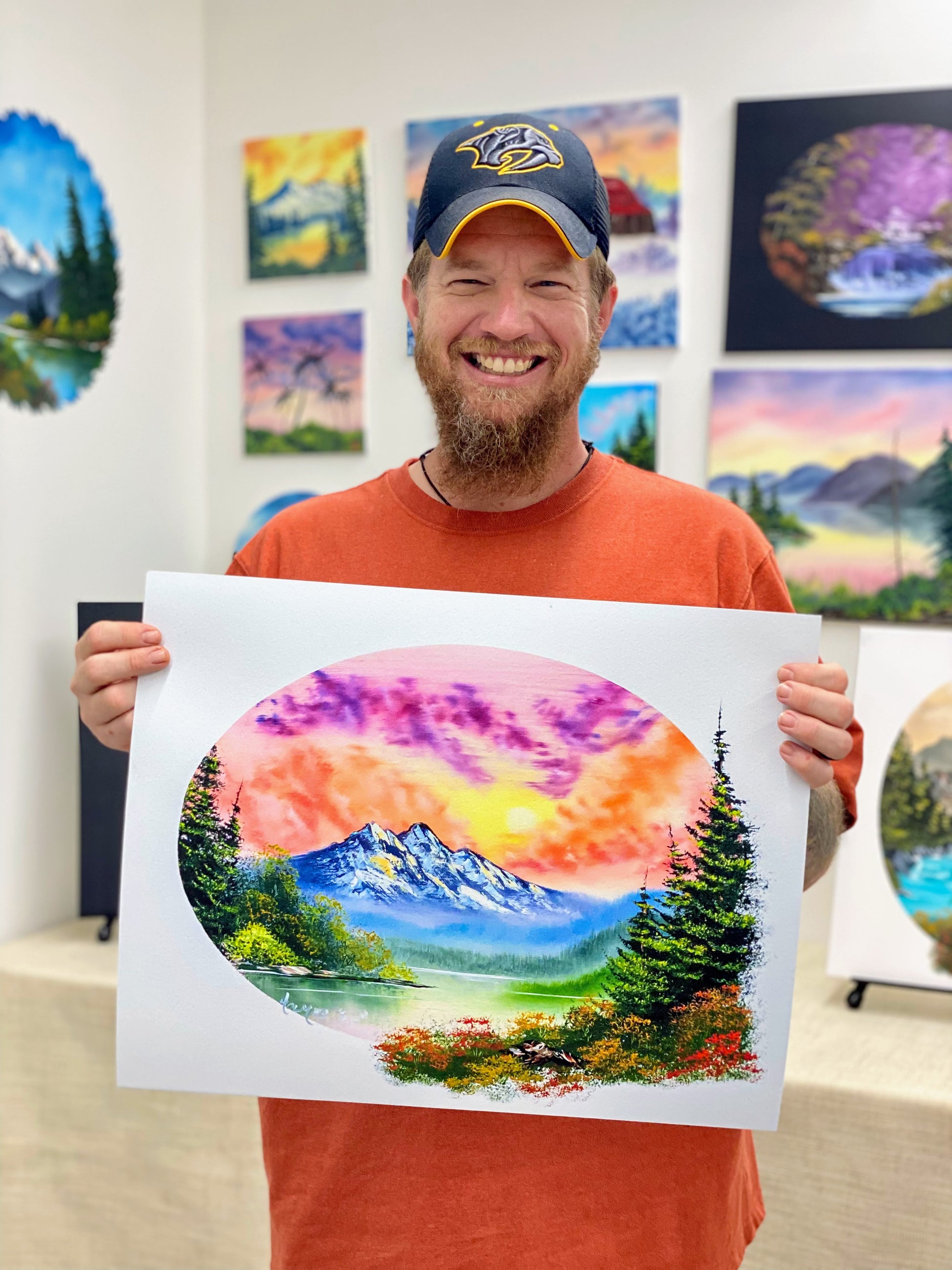 Man holding a painting of a mountain landscape in an art studio