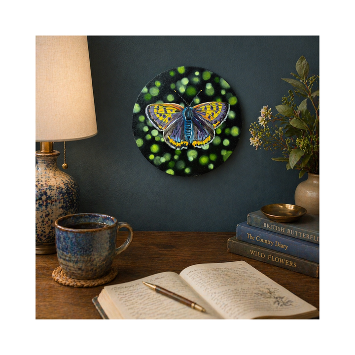 Copper butterfly oil painting on a wall above a desk with books and a cup.