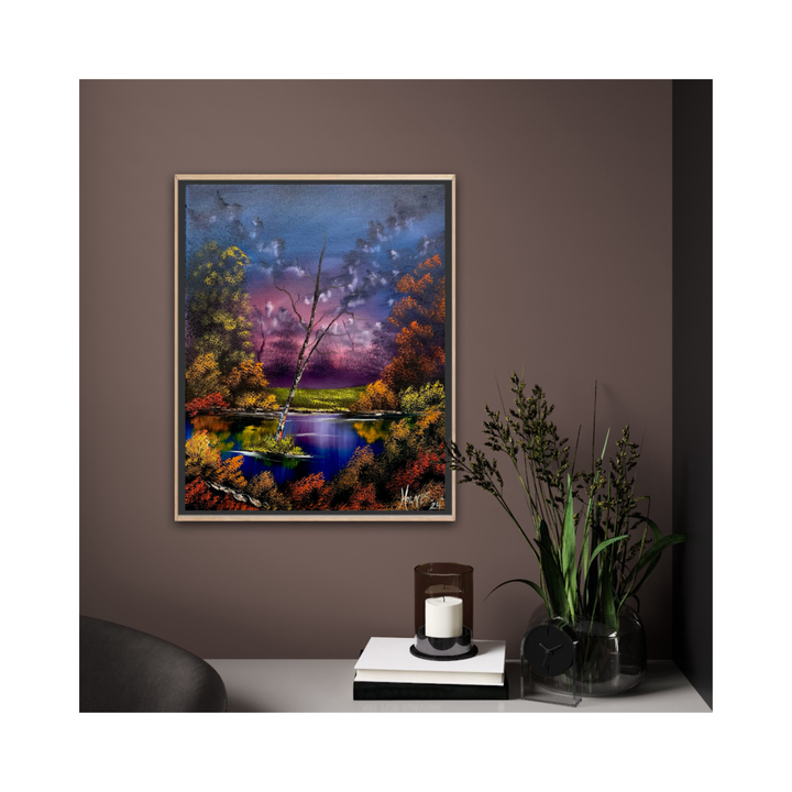 Framed painting of a landscape with a lake on a wall, with a candle and plant on a table below.