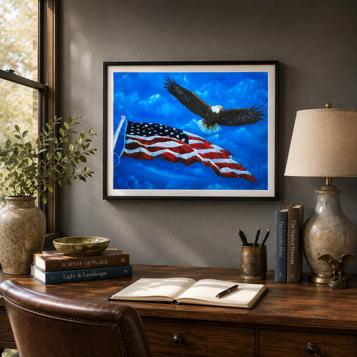 A framed art print depicting a bald eagle flying over an American flag against a bright blue sky, displayed on a dark gray wall above a wooden desk with books, a lamp, and an open notebook.