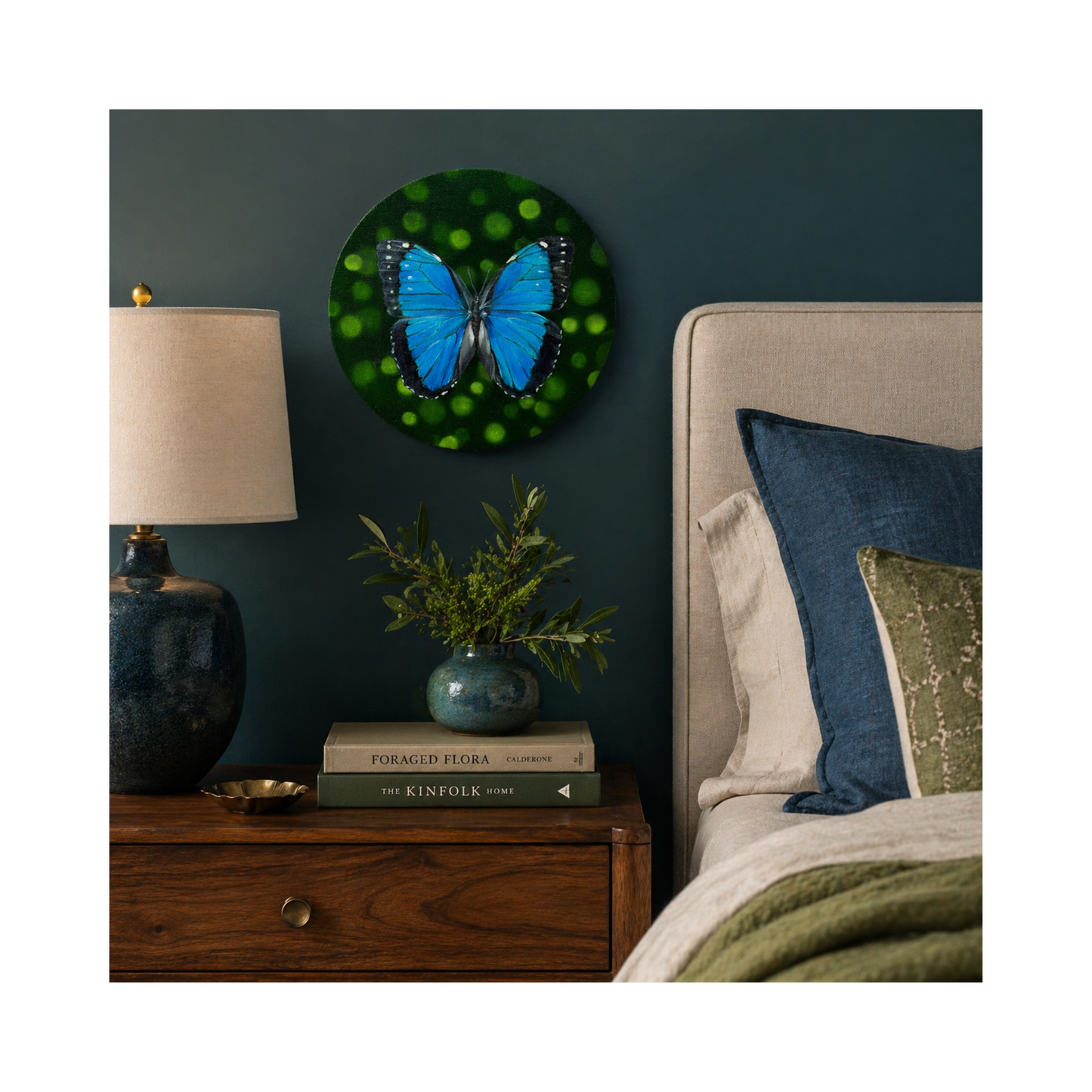 round oil paining of morpho butterfly above a bed and nightstand.