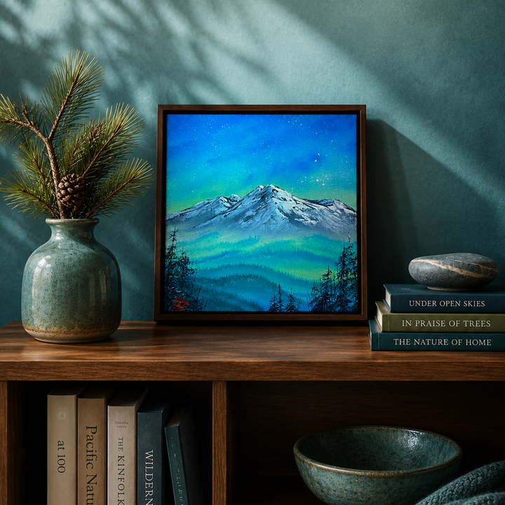 A framed landscape painting of a snow-capped mountain under a vibrant blue and green night sky, styled on a wooden shelf next to a ceramic vase with pine branches and a stack of books.
