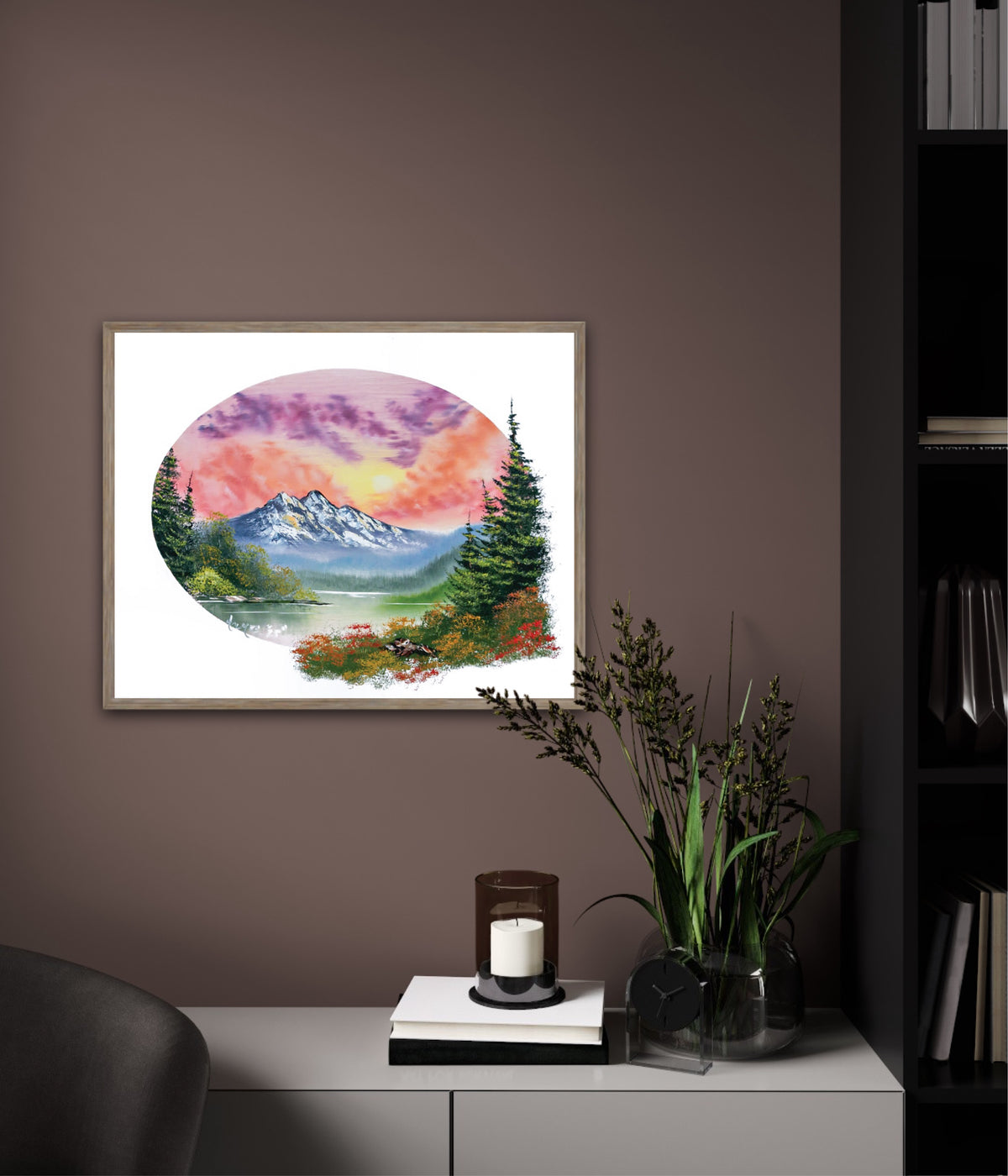 Framed artwork of a mountain landscape on a wall in a room with a plant and candle.
