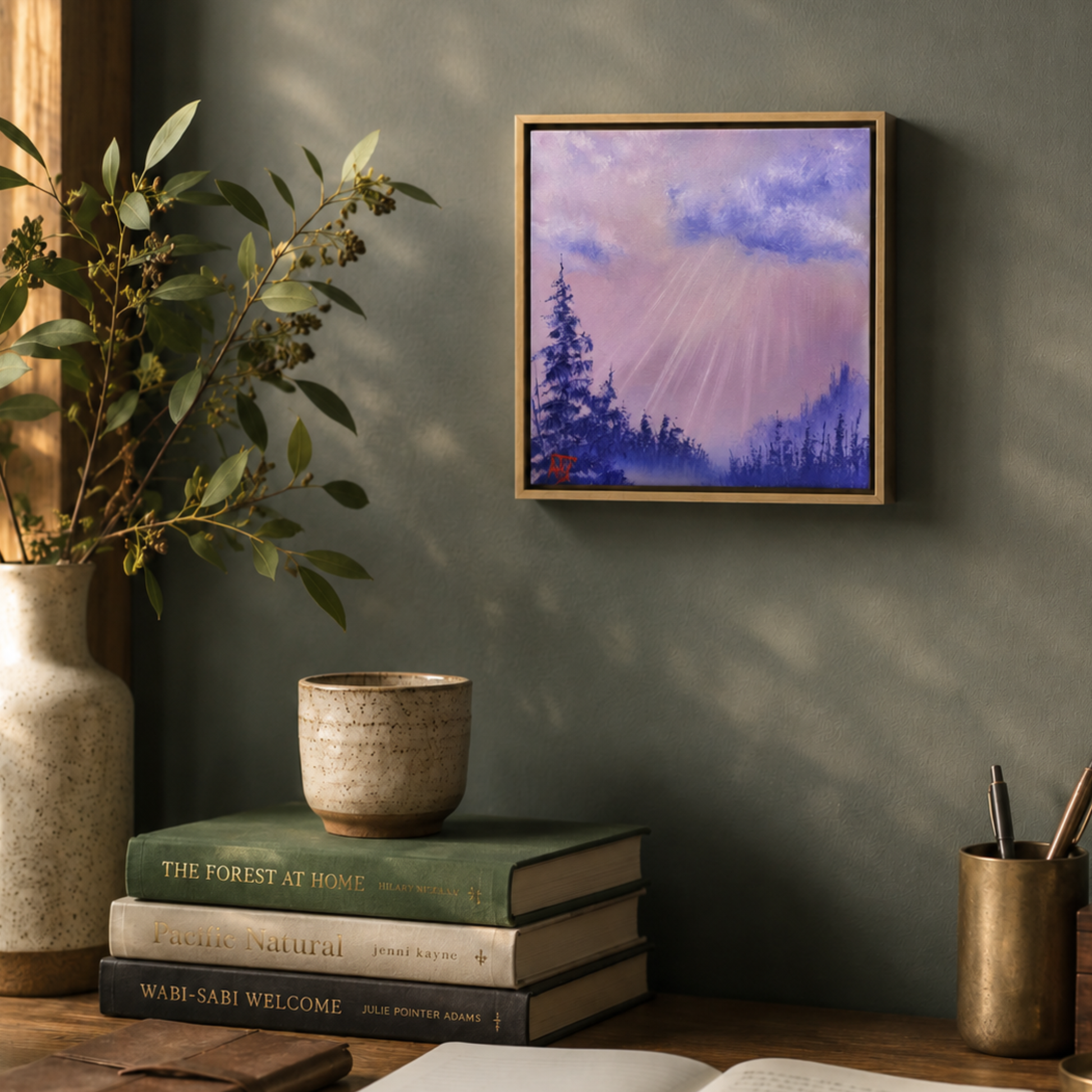 Framed artwork of a purple and pink forest scene on a wall with books and a vase below.
