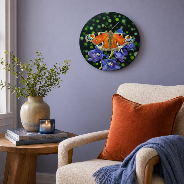 Original oil painting of a peacock butterfly sitting on purple delphinium flowers above a cozy armchair with orange pillow and blue blanket.