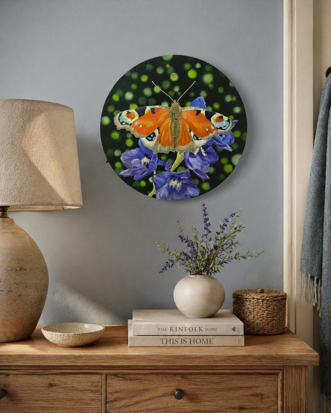 Original oil painting of peacock butterfly sitting on purple delphinium flowers on a gray wall above a wooden dresser.