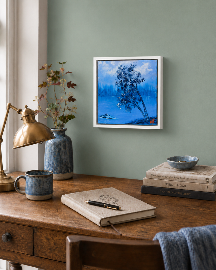 square oil painting of a tree by the lake in a white floater frame displayed on sage wall over writing desk and a journal