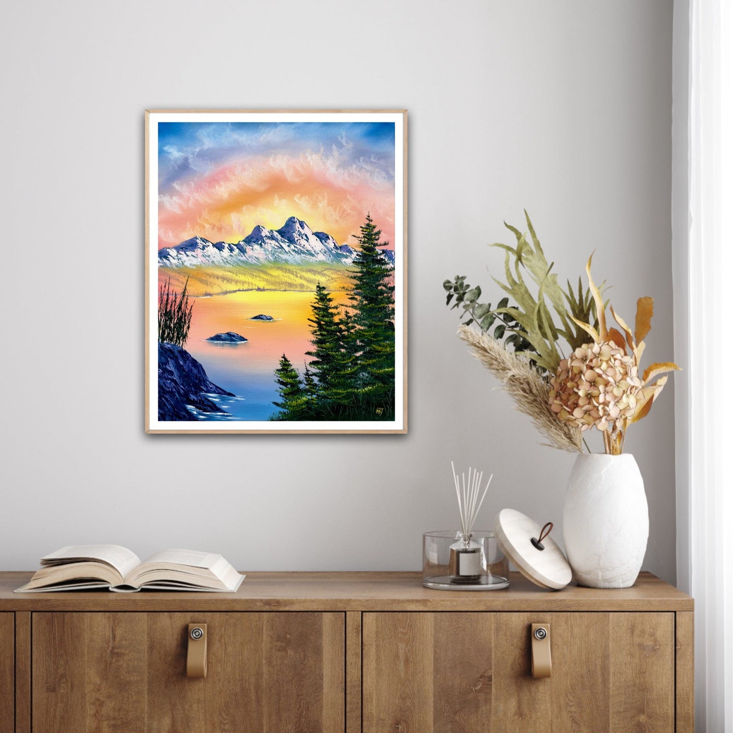 Framed mountain landscape painting on a wall above a wooden cabinet with decor items.