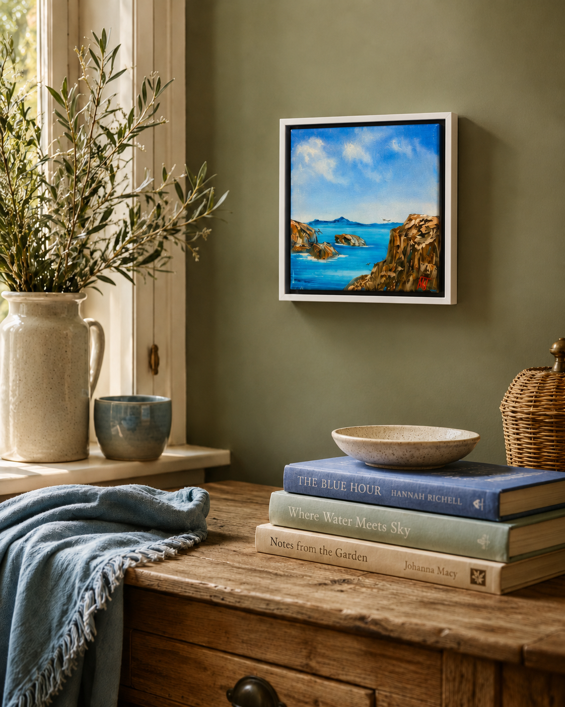 Framed artwork of a coastal scene on a wall above books and decor items.