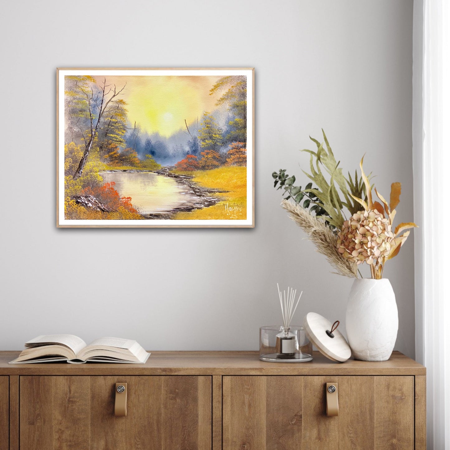Framed landscape painting on a wall above a wooden cabinet with decor items.