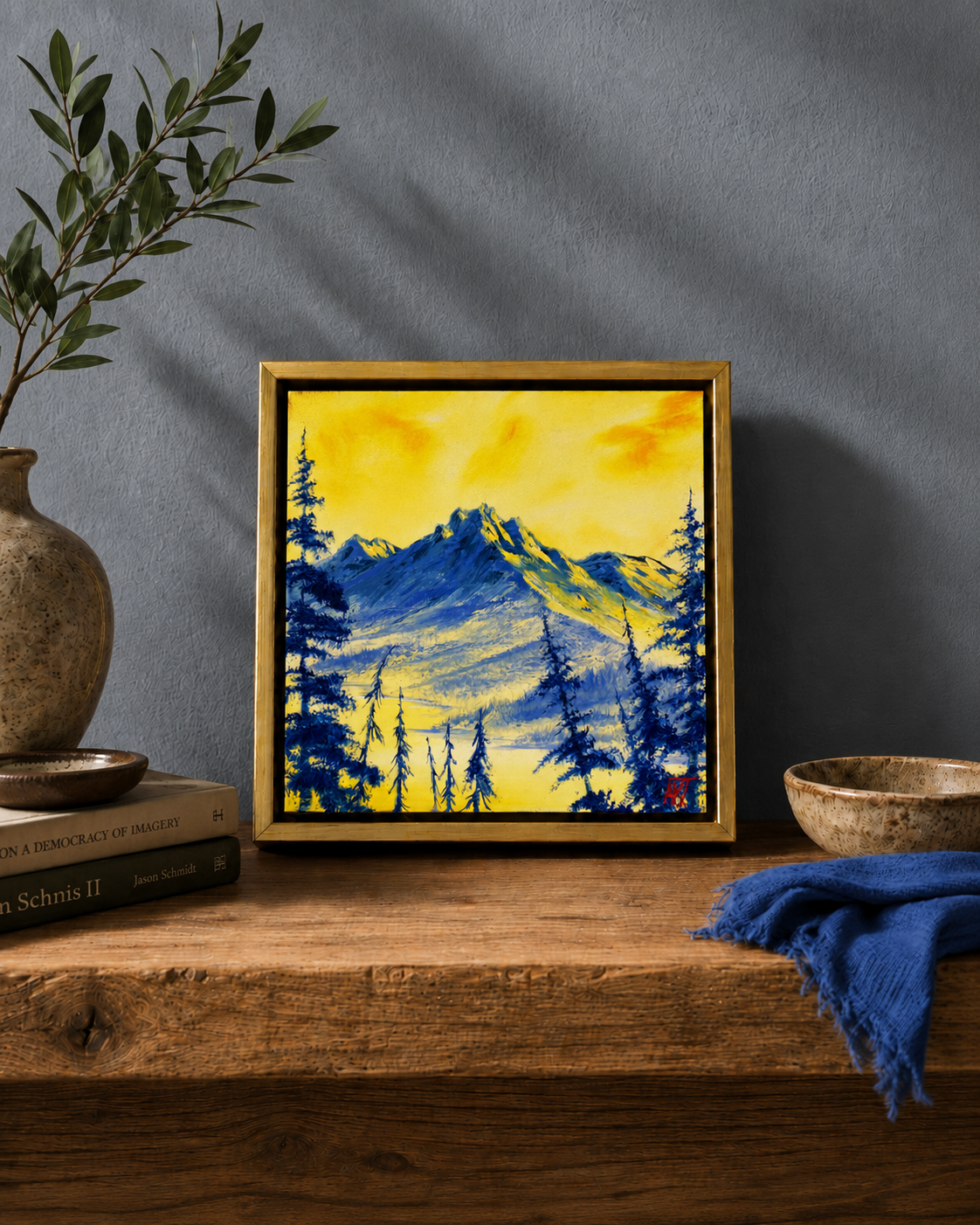 Framed mountain landscape painting on a wooden shelf with a dark wall background