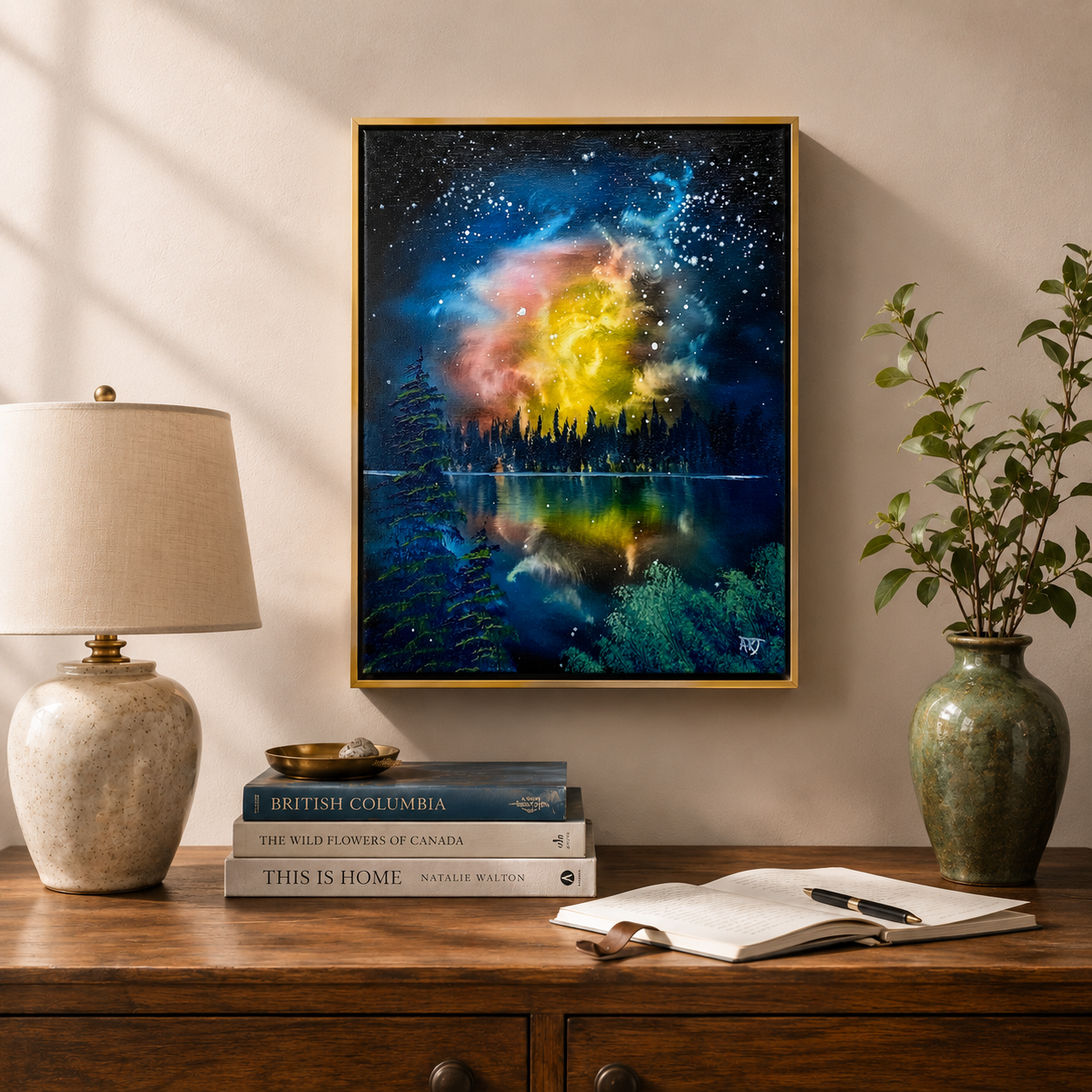 Framed artwork of a colorful galaxy over a lake on a wall above a wooden desk with books and a lamp.