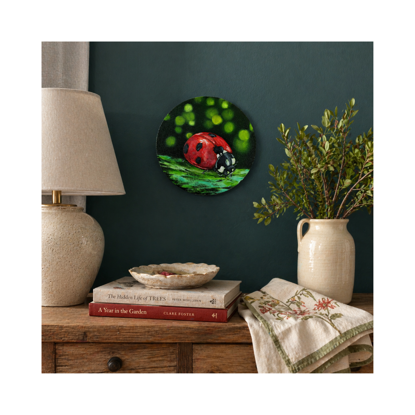 ladybird original oil painting on 8" round canvas over a console with books vase and a lamp
