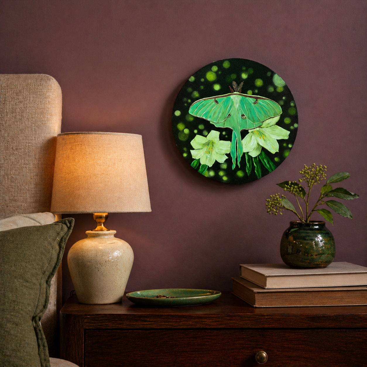Decorative wall art of a green luna moth on white lilly flowers in a room with a lamp and books.