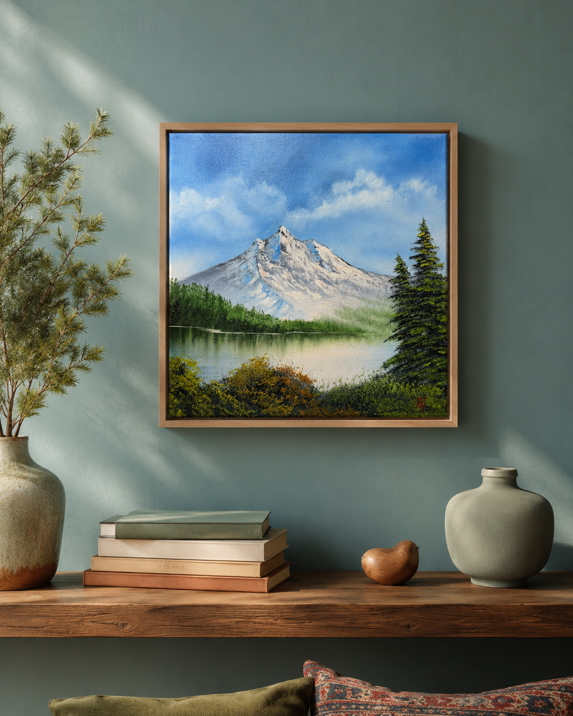 Framed mountain landscape painting on a wall above a wooden shelf with decorative items.