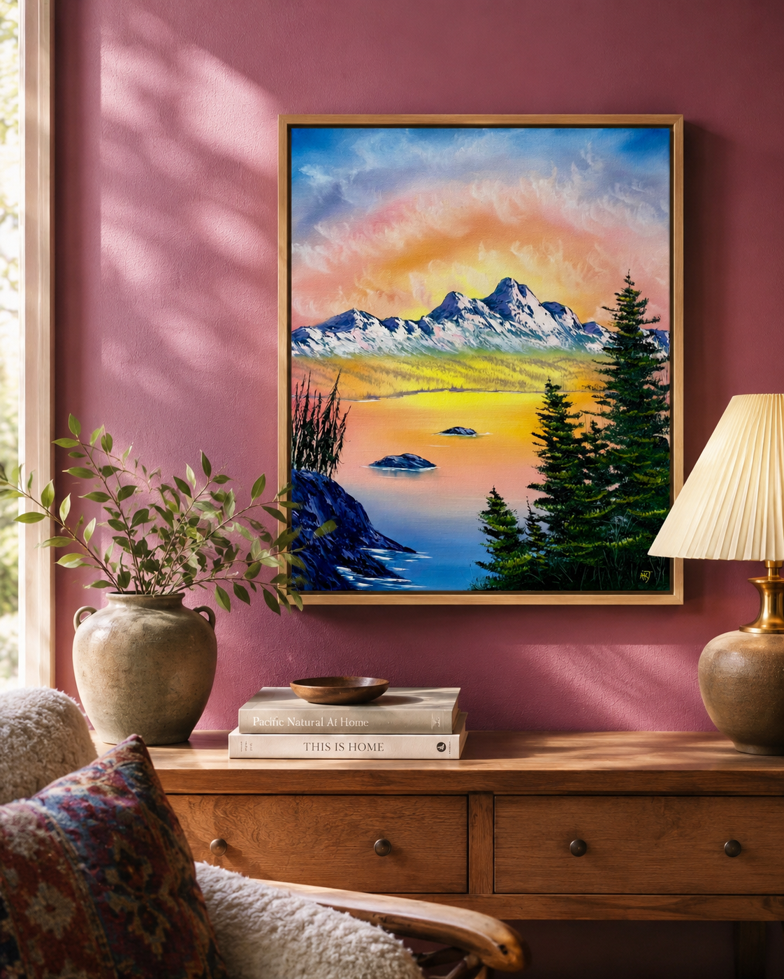 Framed mountain landscape painting on a pink wall above a wooden console table.
